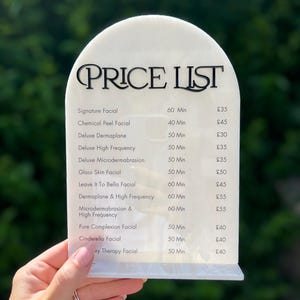 Puede incluir: Una lista de precios de acr&iacute;lico blanco con una parte superior curvada, con texto negro que dice "PRICE LIST". La lista detalla varios tratamientos faciales, incluyendo Signature Facial, Chemical Peel Facial y Deluxe Dermaplane, con los tiempos asociados.