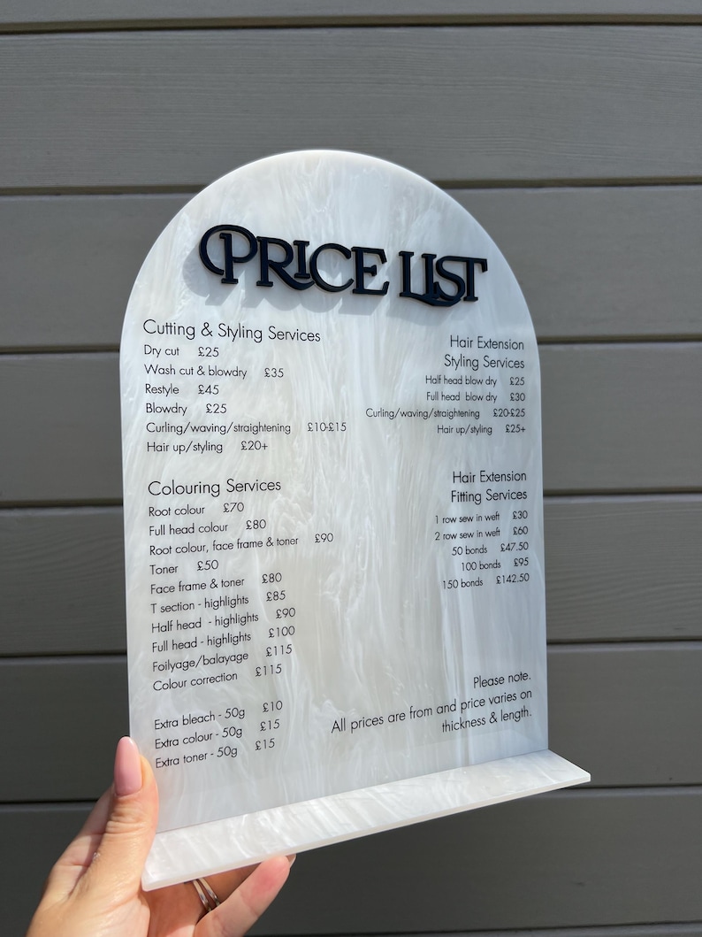 Puede incluir: Una lista de precios de sal&oacute;n de belleza en acr&iacute;lico blanco y negro. El letrero tiene una parte superior arqueada con la inscripci&oacute;n "PRICE LIST" en negro. La lista incluye servicios de corte, peinado, coloraci&oacute;n y extensiones de cabello.