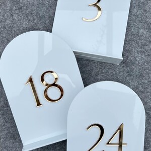 May include: Three white acrylic table numbers with gold numbers. The numbers are 3, 18, and 24.