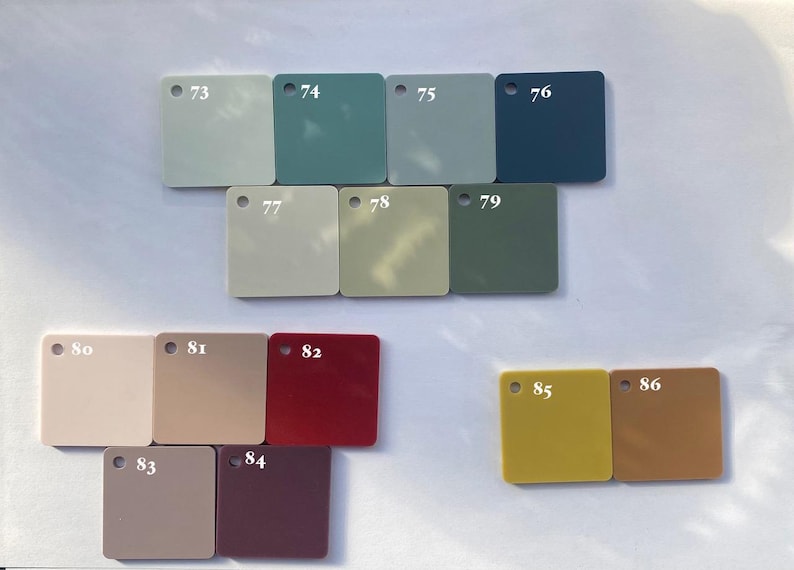 May include: A collection of 12 color swatches, numbered 73 through 86, arranged in rows. The swatches are square and made of a smooth, opaque material. The colors range from light blue to dark red.