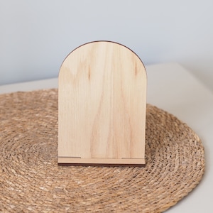 May include: A wooden arch-shaped sign with a natural wood finish. The sign is sitting on a woven straw mat.