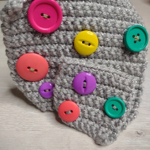 May include: A gray crocheted hat with colorful buttons. The buttons are pink, yellow, purple, red, and green.