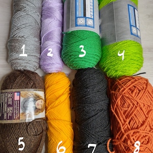 May include: A collection of eight yarn skeins in various colors, including gray, lavender, green, lime green, brown, yellow, black, and orange. The yarn is labeled with details about the material and weight, with one label showing 142 g and 230 m.