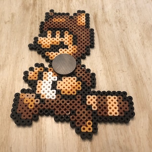 May include: A brown and white pixel art character with a brown hat and a black background. The character is running and has a brown and white striped tail.