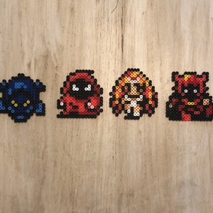 Puede incluir: Cuatro personajes de pixel art hechos con cuentas de colores. Los personajes son una criatura azul y negra, una criatura roja, un personaje femenino con cabello rojo y un vestido blanco, y una criatura roja y negra.