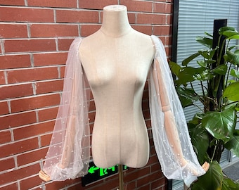 May include: White sheer long-sleeved blouse with pearl embellishments on the sleeves. The blouse is on a white mannequin.