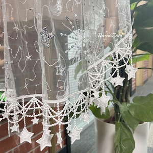 May include: White sheer fabric with a star pattern and a white lace trim. The fabric is decorated with sequins and beads.