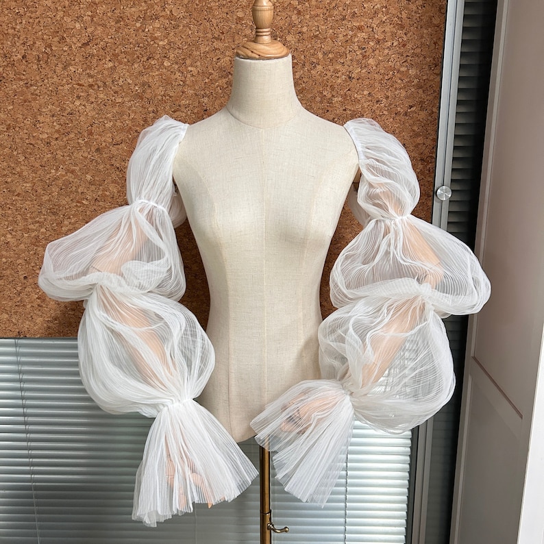 May include: White sheer fabric sleeves with a gathered, puffed design. The sleeves are made of a lightweight, airy material and have a delicate, feminine look.