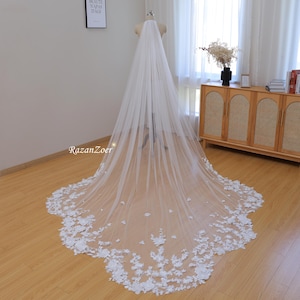 May include: A white bridal veil with a long, flowing train and a delicate floral lace trim. The veil is made of soft tulle and features 3D floral appliques.