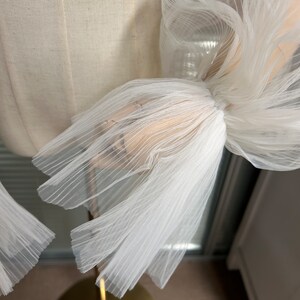 May include: White tulle fabric with a gathered and pleated design. The fabric is soft and delicate, with a slightly sheer appearance.