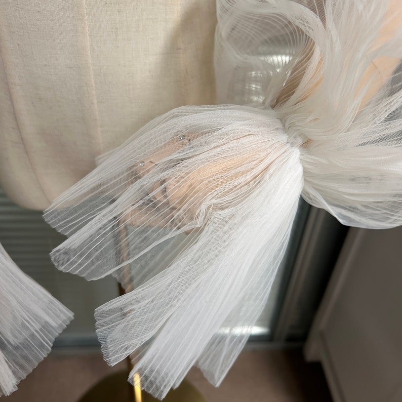May include: White tulle fabric with a gathered and pleated design. The fabric is soft and delicate, with a slightly sheer appearance.