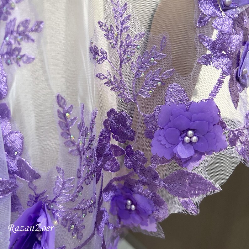 May include: Close-up of a sheer fabric adorned with intricate purple floral embroidery. The design features 3D flowers with pearl-like centers and delicate leaf patterns. The fabric is a light, airy material, perfect for bridal or formal wear.