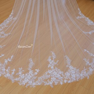 May include: A white bridal veil with a delicate floral lace trim. The veil is made of soft tulle and has a flowing, elegant design.