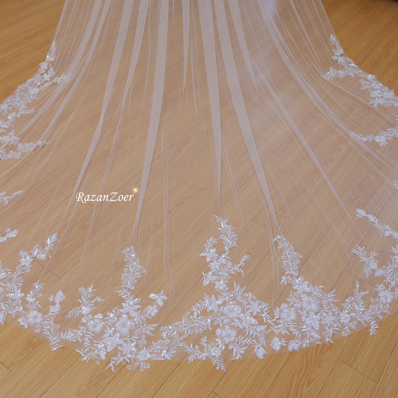 May include: A white bridal veil with a delicate floral lace trim. The veil is made of soft tulle and has a flowing, elegant design.