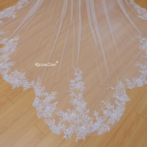 May include: A white bridal veil with a scalloped edge and floral lace trim. The lace is embellished with sequins and beads.