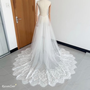 Peut inclure: Une robe de mariée blanche avec une longue traîne fluide. La robe est présentée sur un mannequin. La traîne présente une délicate bordure en dentelle le long de l'ourlet. La robe est en tissu transparent.