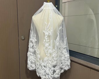 May include: White bridal veil with delicate floral lace trim and scattered rhinestones. The veil is displayed on a mannequin.