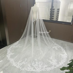 May include: A white bridal veil with a delicate floral pattern. The veil is made of soft tulle and has a long, flowing train.