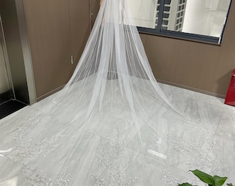 May include: A long, white bridal veil with a delicate beaded design. The veil is made of soft tulle and has a cathedral length.