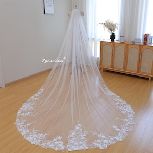 Puede incluir: Un velo de novia blanco largo con un borde de encaje floral. El velo está hecho de tul suave y presenta delicadas flores 3D.