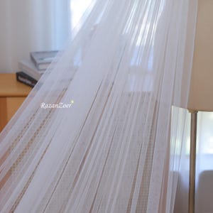 May include: White sheer fabric canopy with a delicate, flowing texture. The fabric is draped over a wooden frame, creating a soft and airy atmosphere.