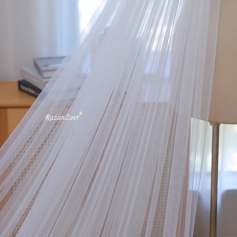 May include: White sheer fabric canopy with a delicate, flowing texture. The fabric is draped over a wooden frame, creating a soft and airy atmosphere.