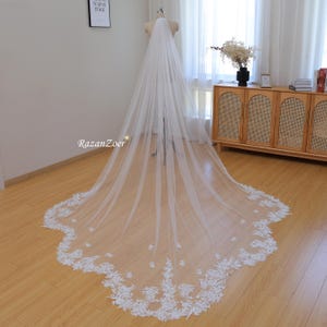 May include: A long, white bridal veil with a scalloped edge and delicate floral lace trim. The veil is made of soft tulle and is perfect for a wedding ceremony.