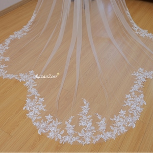 May include: A white bridal veil with a delicate floral lace trim. The veil is made of soft tulle and has a scalloped edge.