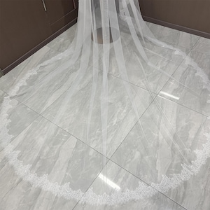 May include: A long, white bridal veil with a delicate lace trim along the edge. The veil is made of a sheer fabric, creating a flowing and elegant look. The lace trim adds a touch of detail to the design.