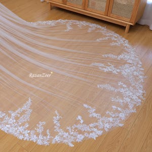 May include: A white bridal veil with delicate floral lace trim. The veil is made of soft tulle and features a scalloped edge.