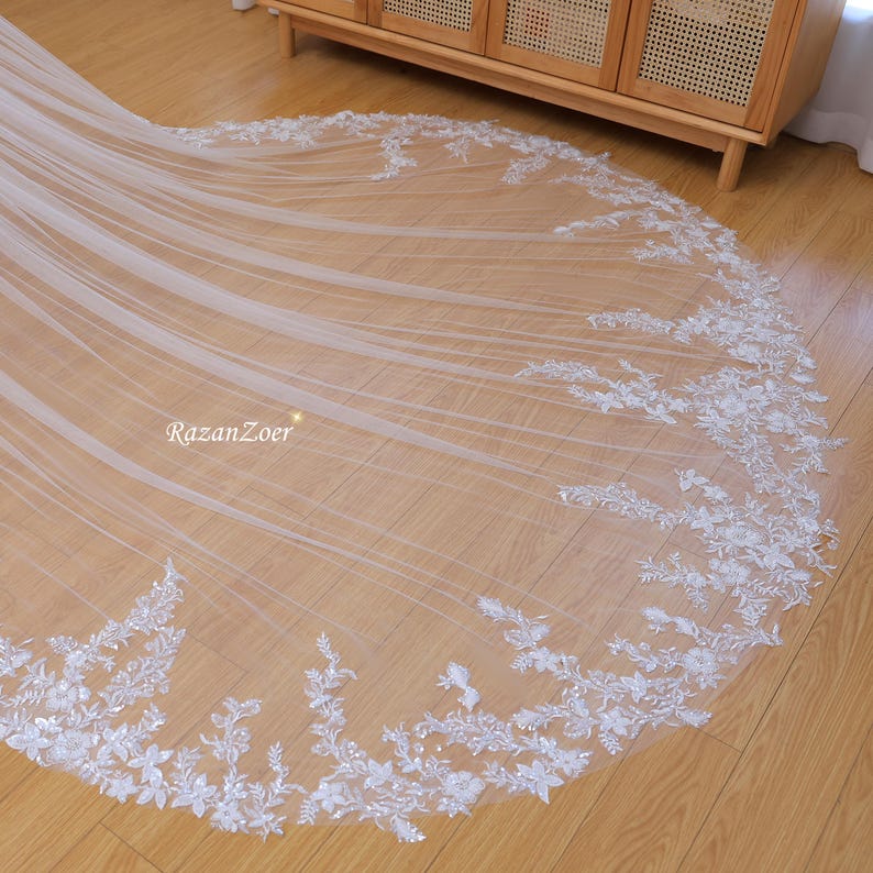 May include: A white bridal veil with delicate floral lace trim. The veil is made of soft tulle and features a scalloped edge.