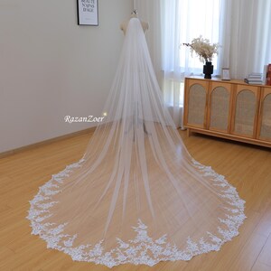 May include: A long white bridal veil with a delicate lace trim. The veil is made of soft tulle and has a scalloped edge.