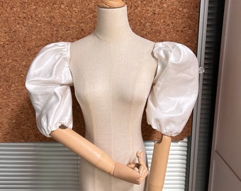 May include: A white satin blouse with puffed sleeves on a dress form.