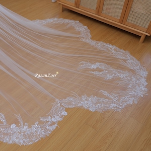 May include: A white bridal veil with a delicate floral lace trim. The lace features small white flowers and leaves, and is accented with sparkling beads.