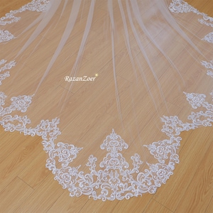 Puede incluir: Un velo de novia blanco con un delicado borde de encaje. El encaje presenta un diseño floral con intrincados detalles.