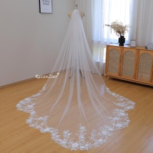May include: A long, white bridal veil with a delicate floral lace trim. The veil is made of soft tulle and has a cathedral length.