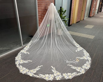 May include: A white bridal veil with a floral design. The veil is made of tulle and has a scalloped edge. The floral design is made of white and yellow flowers.