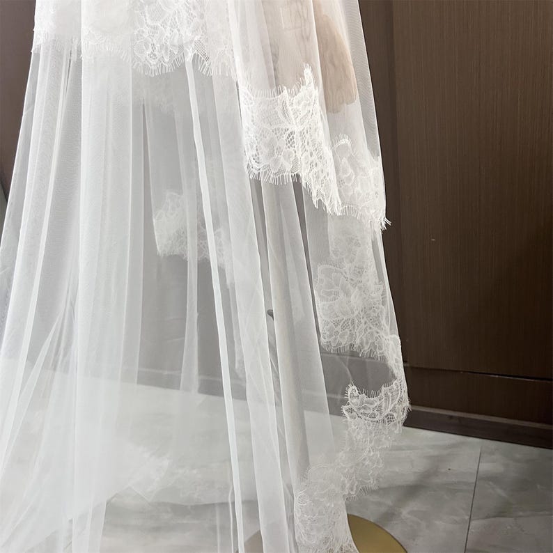 May include: A white bridal veil with delicate lace trim. The veil is made of a sheer, flowing fabric, and the lace adds a touch of elegance. The veil is designed for a wedding or special occasion.
