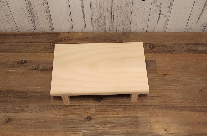 Puede incluir: Una plataforma simple de madera clara con una parte superior rectangular y cuatro patas. La plataforma est&aacute; hecha de madera sin terminar y tiene un patr&oacute;n de veta natural.