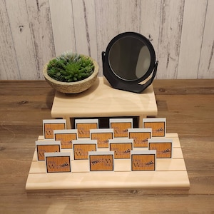 Puede incluir: Un expositor de madera con varias tarjetas cuadradas blancas con el texto "Hey Woodcraft" y un peque&ntilde;o logotipo marr&oacute;n. El expositor tiene dos niveles y un peque&ntilde;o espejo redondo en el nivel superior.