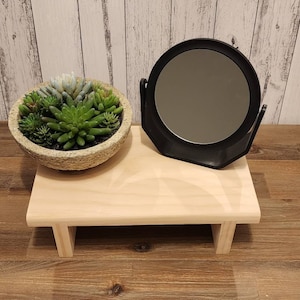 Puede incluir: Una peque&ntilde;a estanter&iacute;a de madera con un espejo redondo y una planta suculenta en una maceta de piedra. La estanter&iacute;a est&aacute; sobre un suelo de madera.