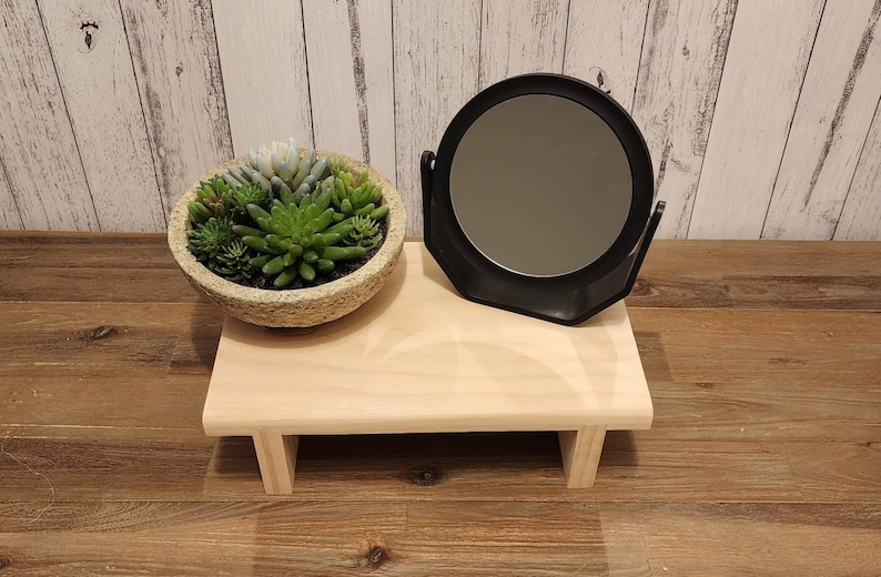 Puede incluir: Una peque&ntilde;a estanter&iacute;a de madera con un espejo redondo y una planta suculenta en una maceta de piedra. La estanter&iacute;a est&aacute; sobre un suelo de madera.