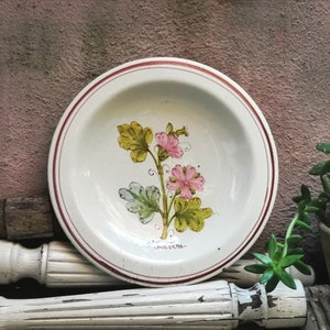 Op de afbeelding: Een wit keramiek bord met een bruine rand en een bloemenmotief met roze bloemen en groene bladeren. Op het bord staat het woord "Savona".