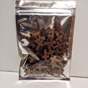 May include: A silver resealable bag filled with a large quantity of small wooden cross shapes. The crosses are a dark brown color.