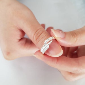 May include: A silver ring featuring a feather design. The ring is adjustable and can be worn on any finger.