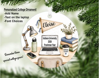 Op de afbeelding: Een rond wit ornament met een bureau-illustratie, een laptop met de tekst Indiana University 2026 Freshman Year, een bureaulamp, een waterfles, een smartphone, drie boeken, een plant in pot en een beker met de tekst COFFEE needed.