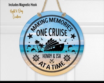 May include: A round hanging sign with a rope hanger featuring a beach and ocean scene. The text reads MAKING MEMORIES ONE CRUISE AT A TIME and HENRY & ISA. Graphics include a cruise ship, palm trees, dolphins, starfish, and ship wheels.