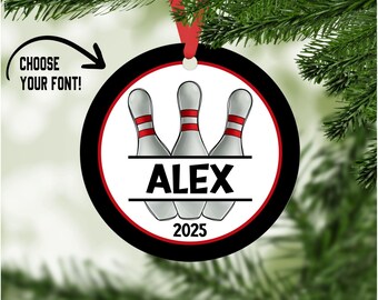 May include: A personalized bowling-themed ornament with a red ribbon for hanging. The ornament features three bowling pins with red stripes, the name "ALEX," and the year "2025." The design is set against a white background with a black border.
