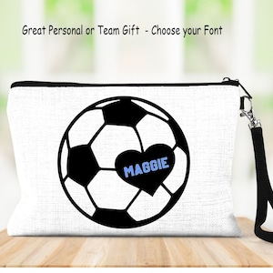May include: White canvas makeup bag with a black soccer ball design and a black heart with the name Maggie in blue text.