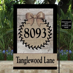 May include: A rectangular garden flag featuring a light wood grain background with a black border. A central burlap-textured circle contains the black number 8093, topped with a brown bow. The bottom section displays the text Tanglewood Lane.